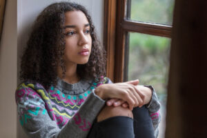 teenage girl sitting in her room by the window looking pensive and wondering if adults are skilled at recognizing self harm in teens