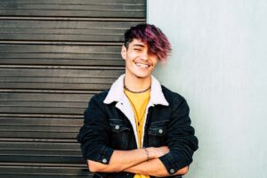 smiling teenager with unconventional hair style leans against door after finding teen mental health treatment in Pasadena