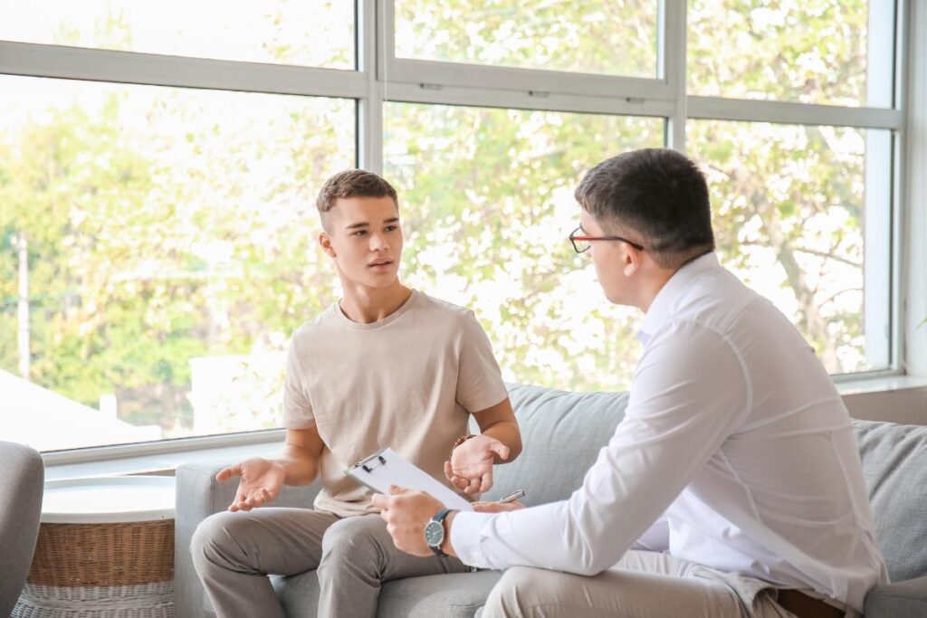 adolescent male seated on couch talking to therapist about the benefits of motivational interviewing for adolescents.