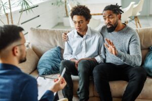 Father and teenage son seted on couch in therapist's office discussing the role of family therapy in adolescent mental health