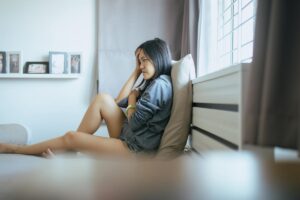 teenager girl seated on her bed in her room looking pensive as she contemplates a schizoaffective disorder treatment program.