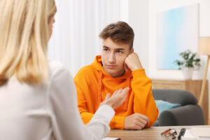 teenage boy in orange hoodie talking to blonde-haired female therapist in an professional office setting about finding intensive outpatient treatment for teens in Pasadena, CA.