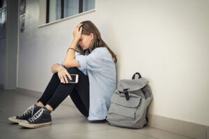 teenage girl leaning against wall looking distraught and hoping her parents learn how to recognize PTSD in your teen and get help.